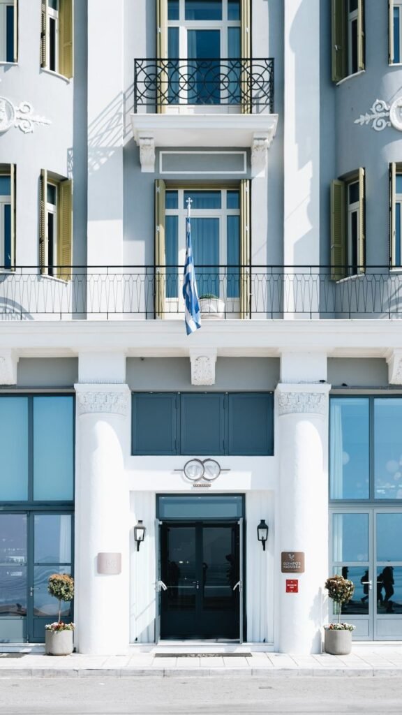 Front view of a boutique hotel facade adorned with a Greek flag, blue accents, and classic columns.